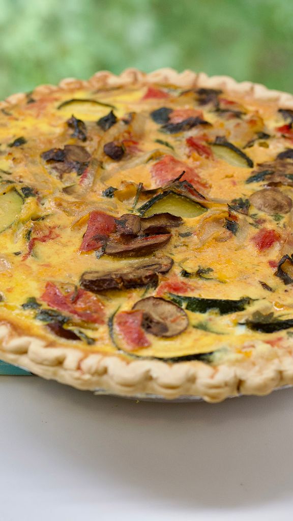 Photo: A bright image of a crusted quiche, with various amounts of vegetables like mushrooms, tomatoes, eggplant, and more. The round quiche sits on a bright, white table.