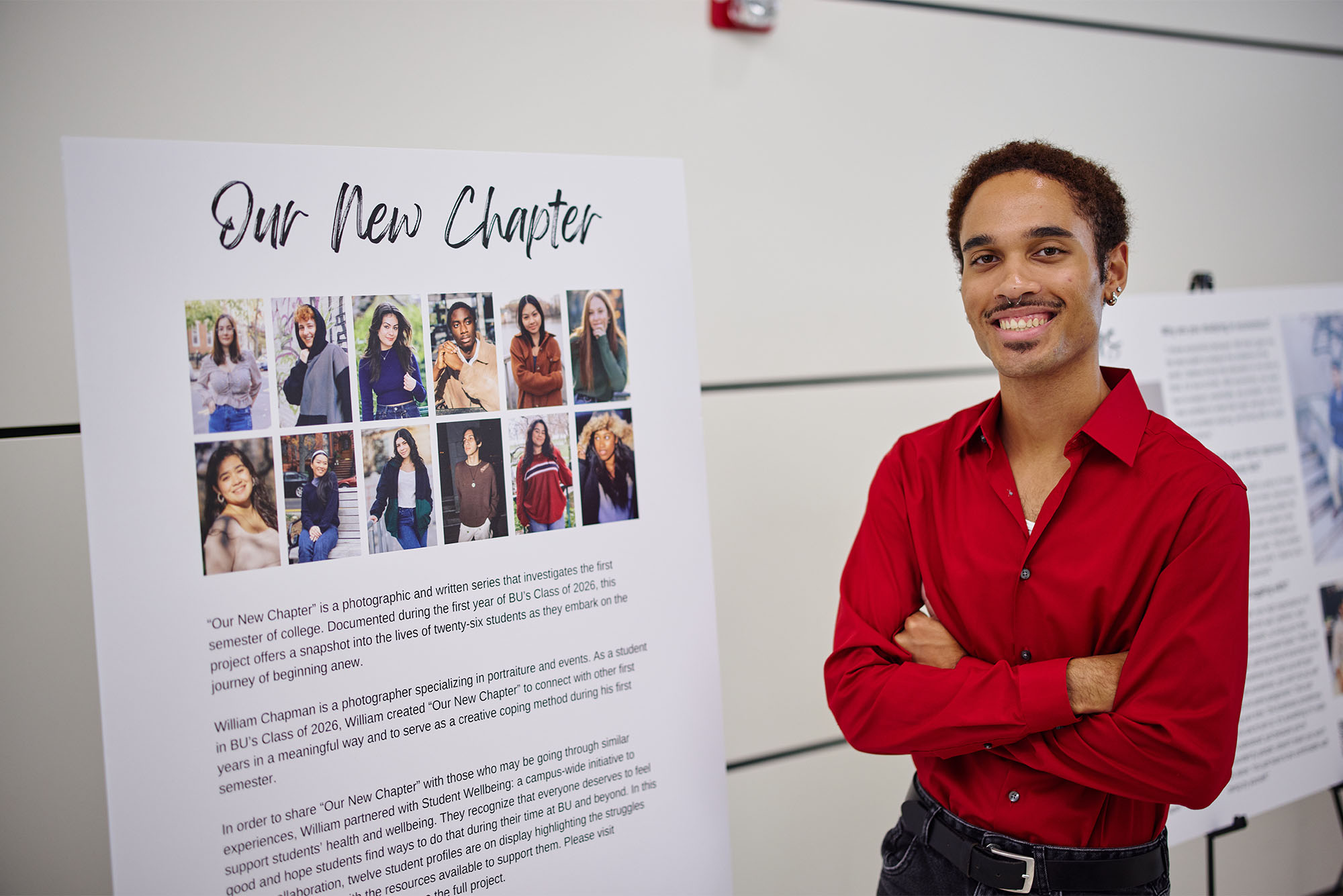Photo: Will Chapman, a young person with short dark hair and a moustache and large smile on their face stands next to a posterboard reading "Our New Chapter" at a recent photography showcase