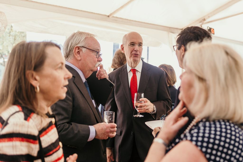 Photo: Bob Brown (left), a white man with grey hair and wearing glasses and a black suit, mingles with Kenneth freeman (right), a tall white man wearing a black suit and red tie, at a reception.