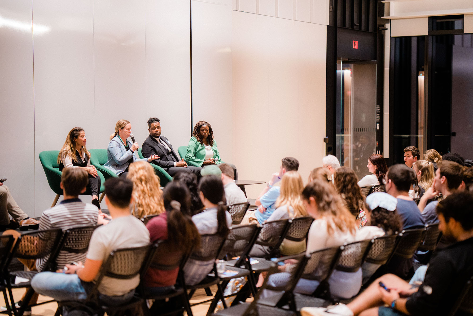 Photo: Boston City Council At-Large candidate forum. On stage sit the four candidates, from left: Julia Mejia, Erin Murphy, Henry Santana, and Ruthzee Louijuene. They sit in chairs and speak into microphones to a small, seated audience.