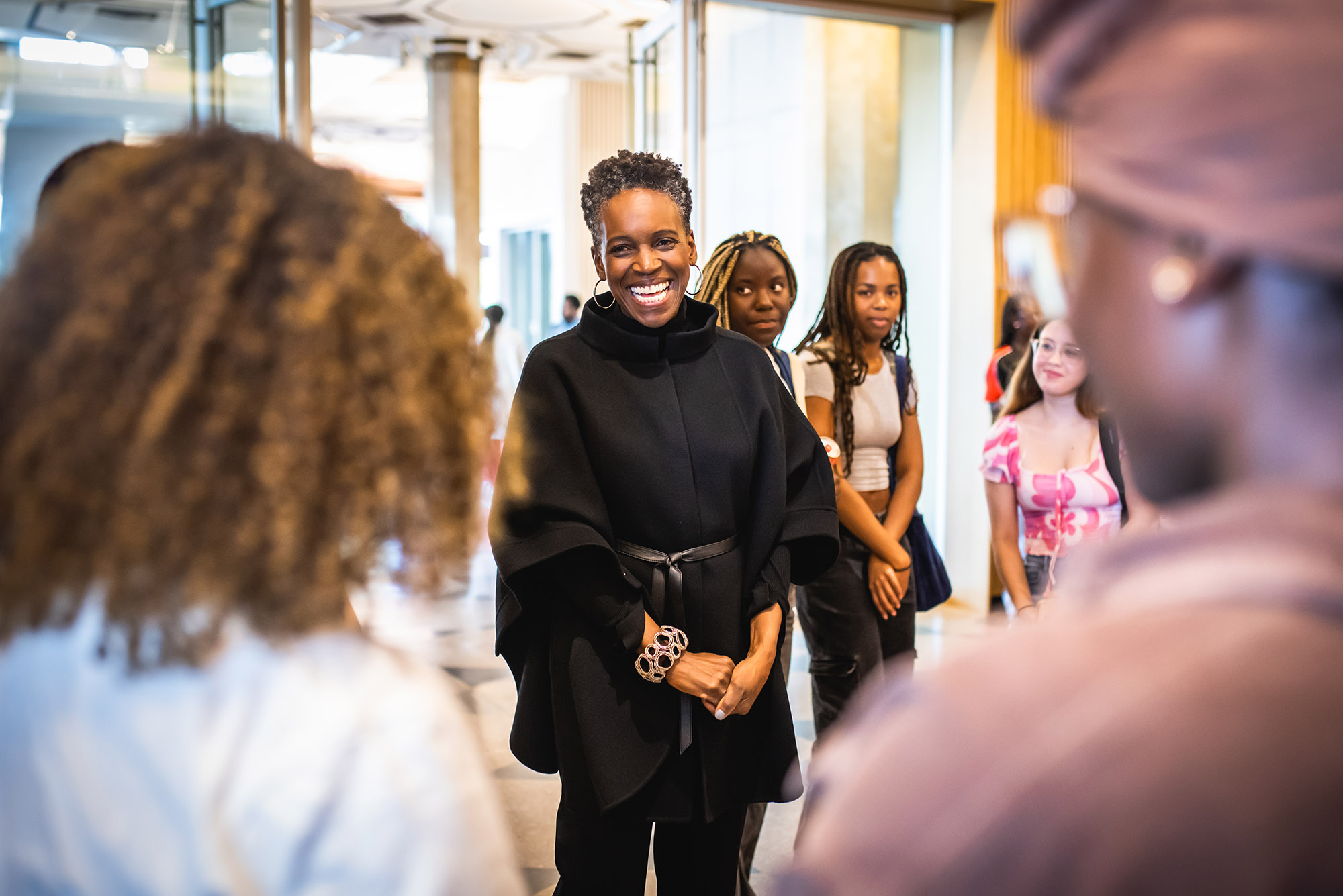 Photo: Melissa Gilliam, a Black woman wearing a black jacket and pants, wrapped up with a meet-and-greet session with students at the Howard Thurman Center. She stands at the center as various diverse students smile and look on.