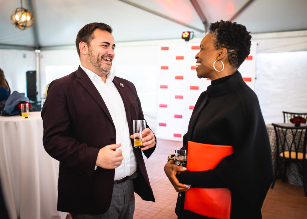 Photo: The new BU president, Melissa L. Gilliam (right), a Black woman wearing a black turtleneck and pants, greets Dean of Students, Jason Campbell-Foster, a white man wearing a white collared shirt and black blazer, during a reception.