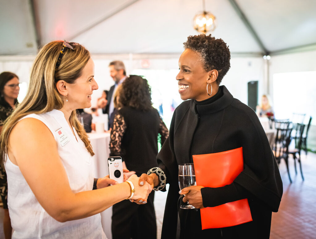Photo: The new BU president, Melissa L. Gilliam (right), a Black woman wearing a black jacket and pants, greets Judy Platt, a white woman with blonde hair wearing a white dress, during a reception.