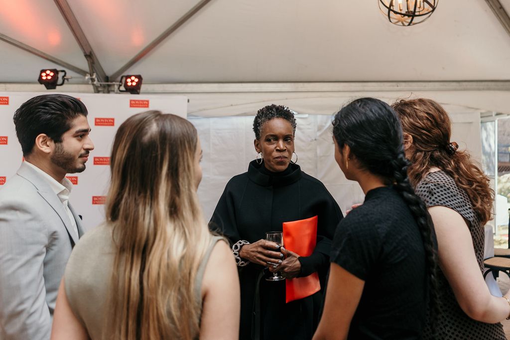 Photo: Gilliam, a Black woman wearing a black jacket and pants, listens to a group of students facing away from the camera. 