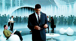 This is a GIF from the men in black movie of famous actor Will Smith. He is in a blue dome room that has random graphics. He has a medium skin tone with short, dark hair. He is wearing a black suit with a white dress shirt and a black tie. He is putting on his black sunglasses with both of his hands while he is smirking.
