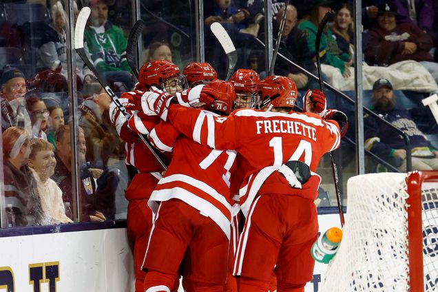 Photo: A group of four men dressed in red BU hockey gear hug and embrace on the ice rink at the end of a game.