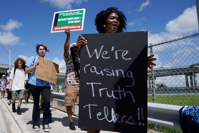 Photo: People carry signs during the "Teach No Lies" march to the School Board of Miami-Dade County to protest Florida's new standards for teaching Black history. A Black woman in the front holds a large black sign with the words "We're raising truth tellers!" in white chalk.