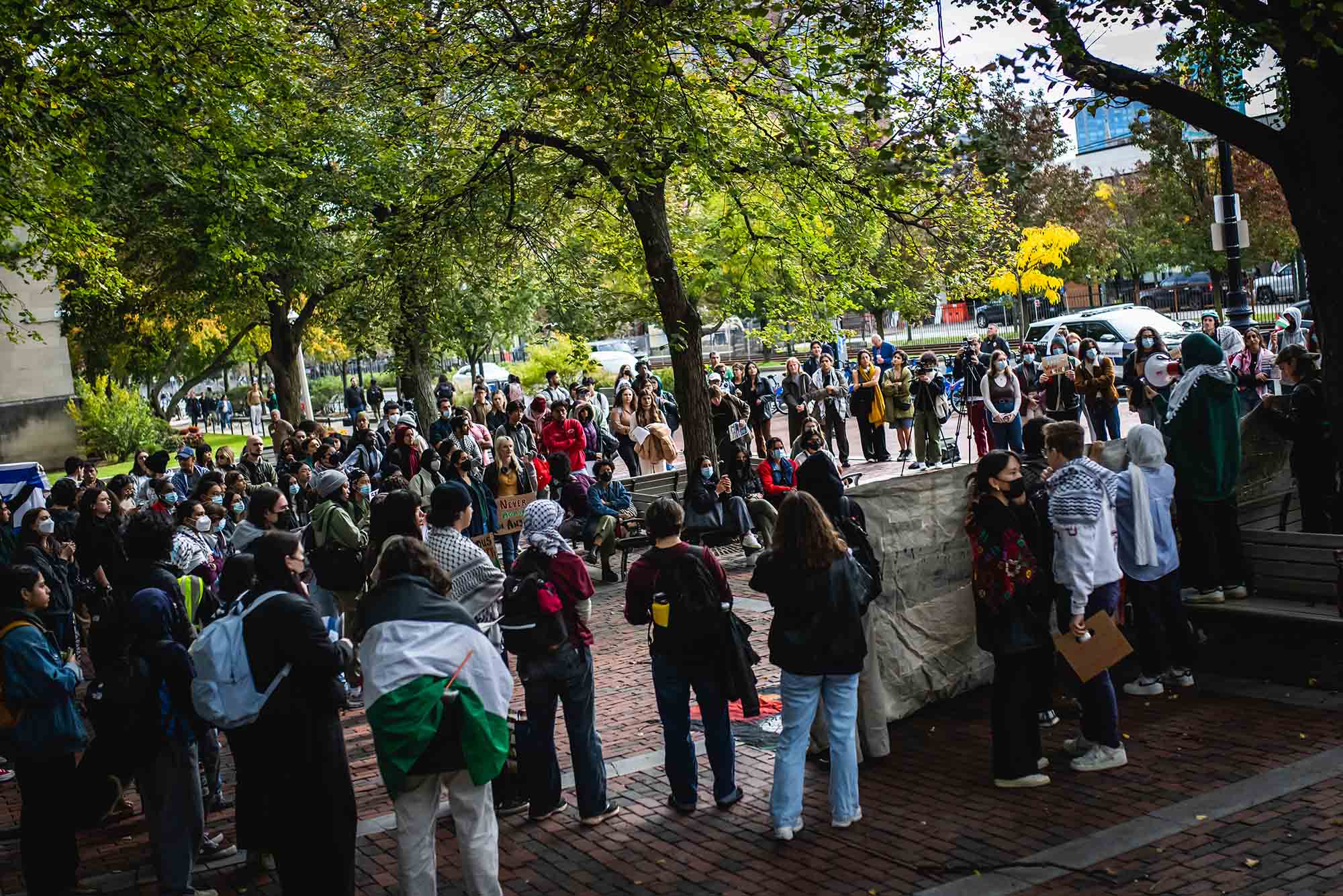 Photo: Students gather outside of the GSU during a walkout in support of Palestine on October 23, 2023. A crowd of students, some holding signs and and flags in support of Palestine, stand together on a cobblestone sidewalk area.