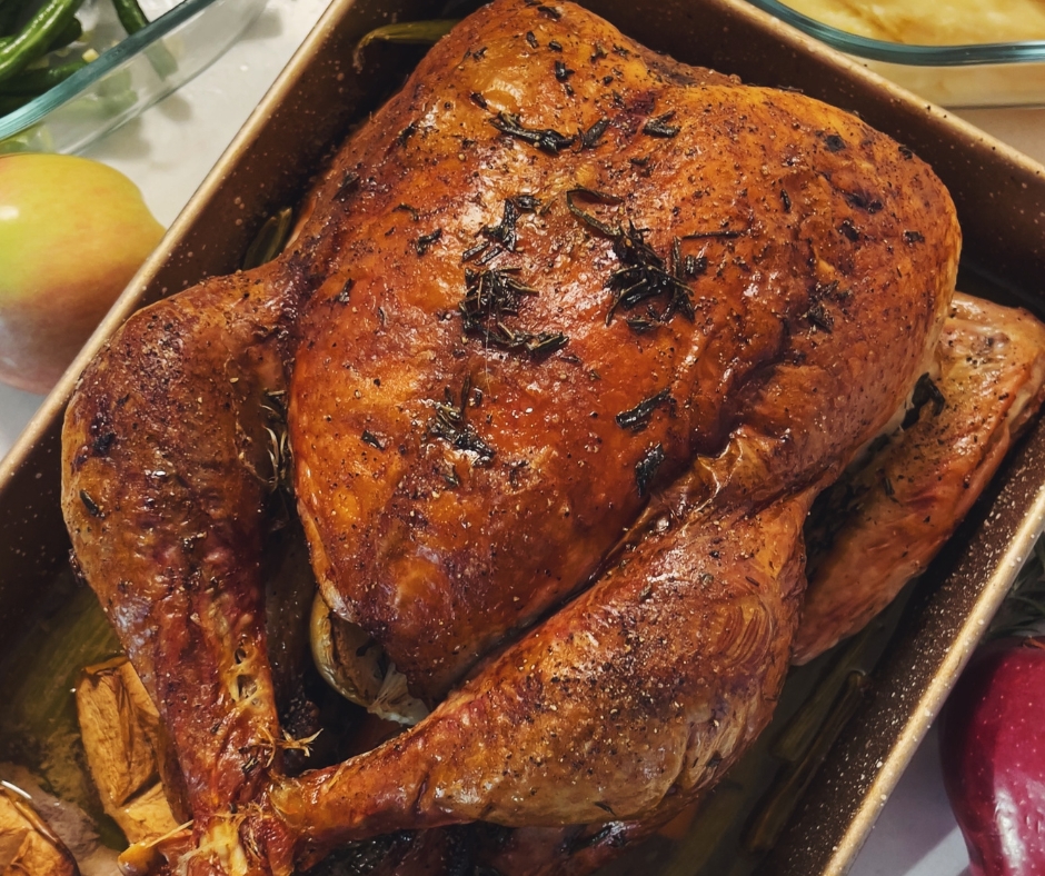 Thanksgiving Turkey that is browned with seasoning on top. It is in a rectangular pan.