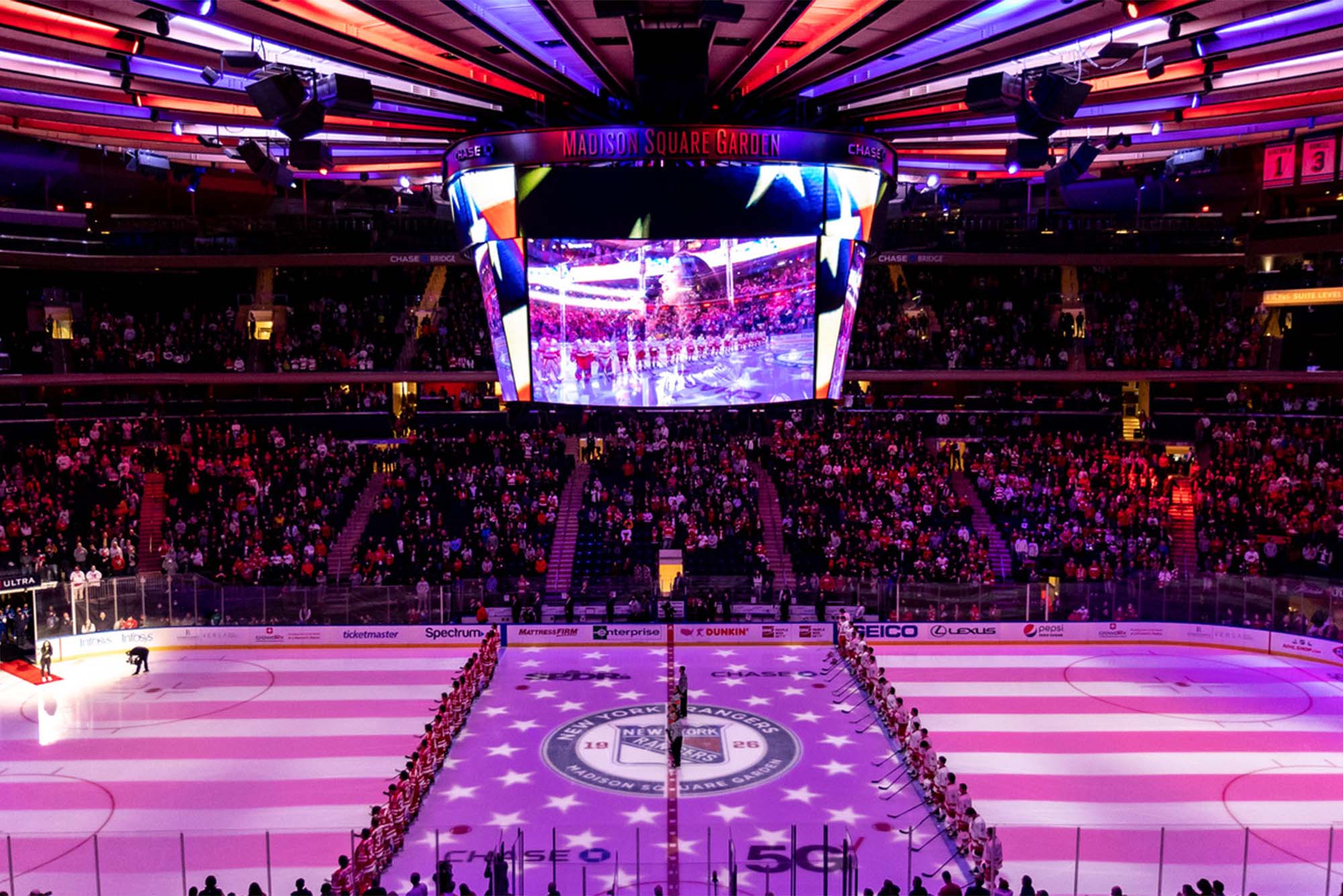 Photo: The interior of Madison Square Garden, packed with people. A large ice rink is visible under a gigantic jumbotron depicting hockey players skating on the ice