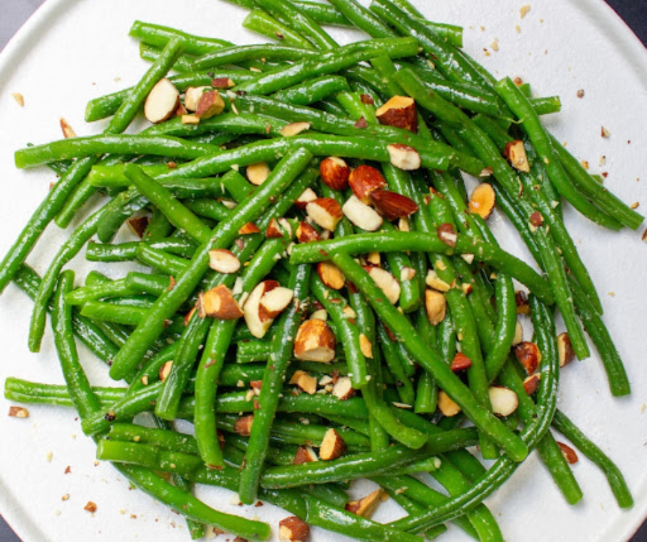 A plate of Greenbeans in a white dish with crushed nuts on top.