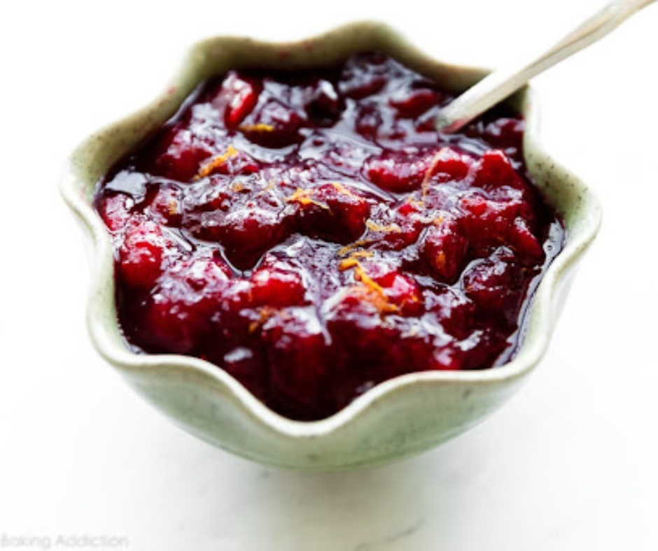 This is a dish of crushed cranberry sauce. There is a silver serving spoon in the sauce and it is in a white star shaped dish.