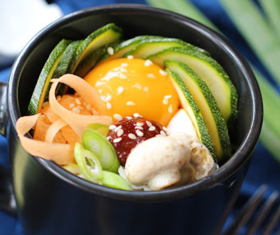 This is a black bowl of bibimbap. It has avocado, mushroom, egg, noodle, and onion.