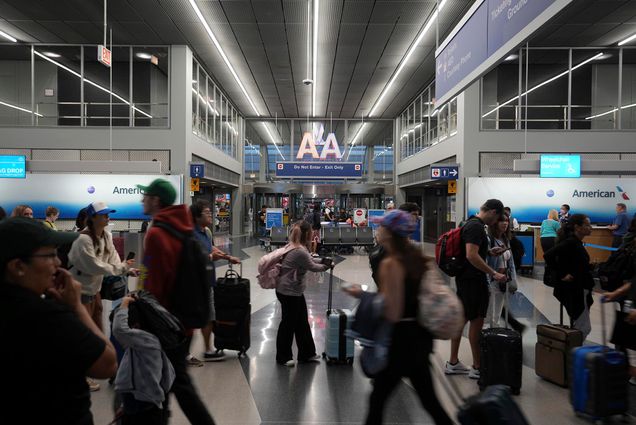 Photo: A large line of people is shown waiting in an airport to check in. Other people are shown walking by with luggage in the busy terminal.