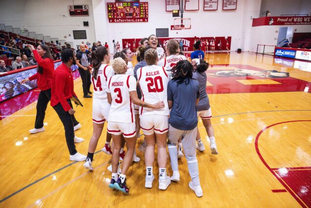 Photo: A group of women's basketball players in red and white jerseys huddle together and appear to be celebrating