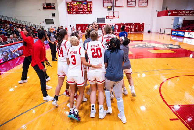 Photo: A group of women's basketball players in red and white jerseys huddle together and appear to be celebrating