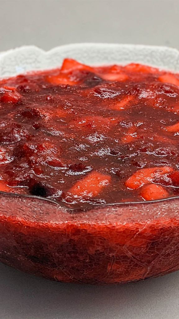 Photo: A clear glass bowl of cranberry sauce with chunks of fruit visible