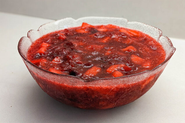 Photo: A clear glass bowl of cranberry sauce with chunks of fruit visible
