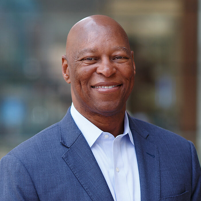 Photo: A bald black man wearing a suit with a large smile poses for a headshot