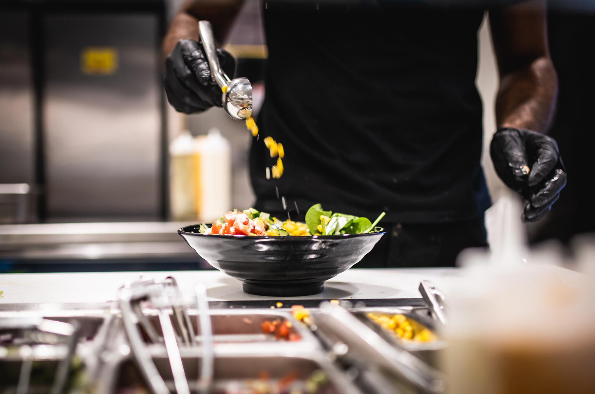 Photo: a Halal Shack bowl of tomatoes, zucchini, corn, and lettuce is shown being made by a worker dressed in all black in a large black bowl.