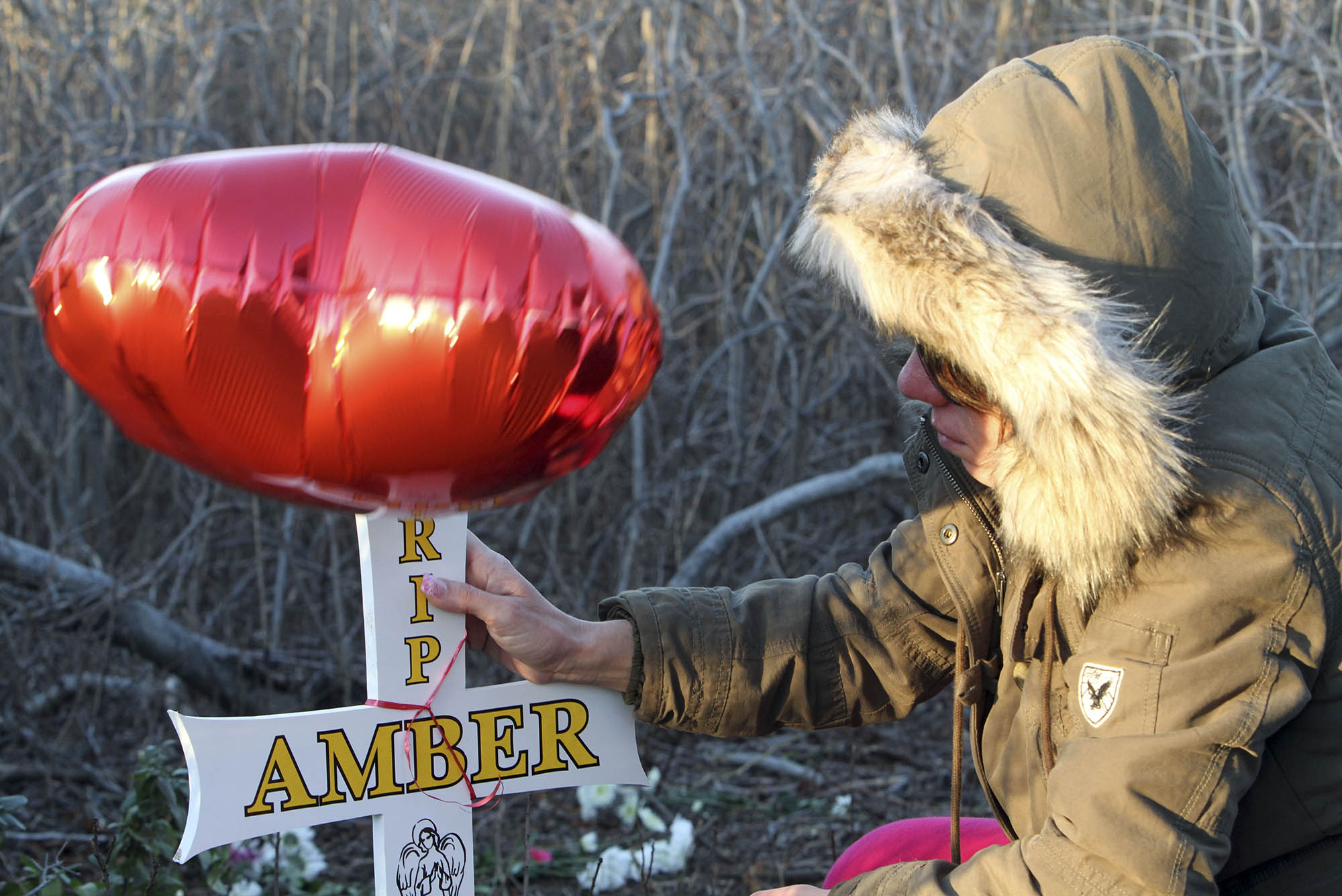 Photo: An image of Kim Overstreet, sister of Amber Lynn Costello, fixing a cross stuck into the ground as a memorial for her sister. There is a foil heart balloon on top.