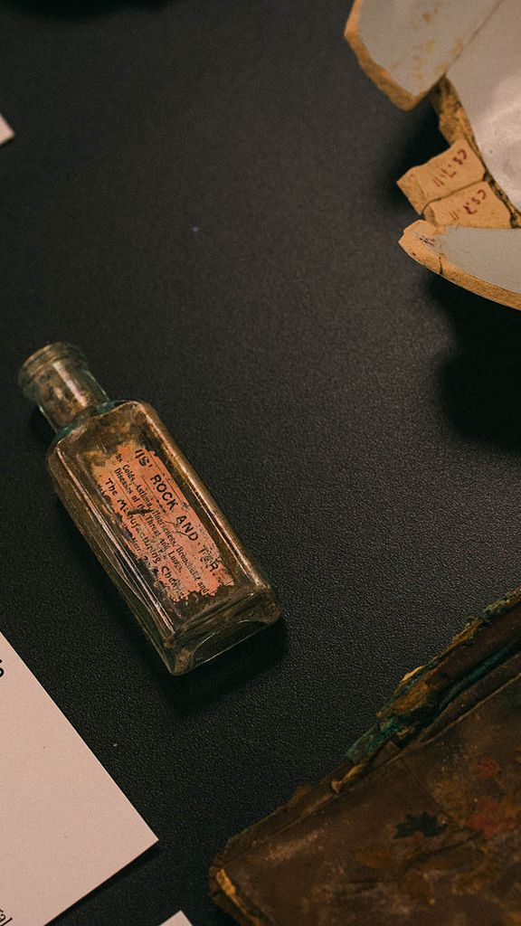Photo: An overhead shot of a few items on display at the Mary C. Beaudry Community Archaeology Center. An old glass medicine bottle is featured in the center of a black table.