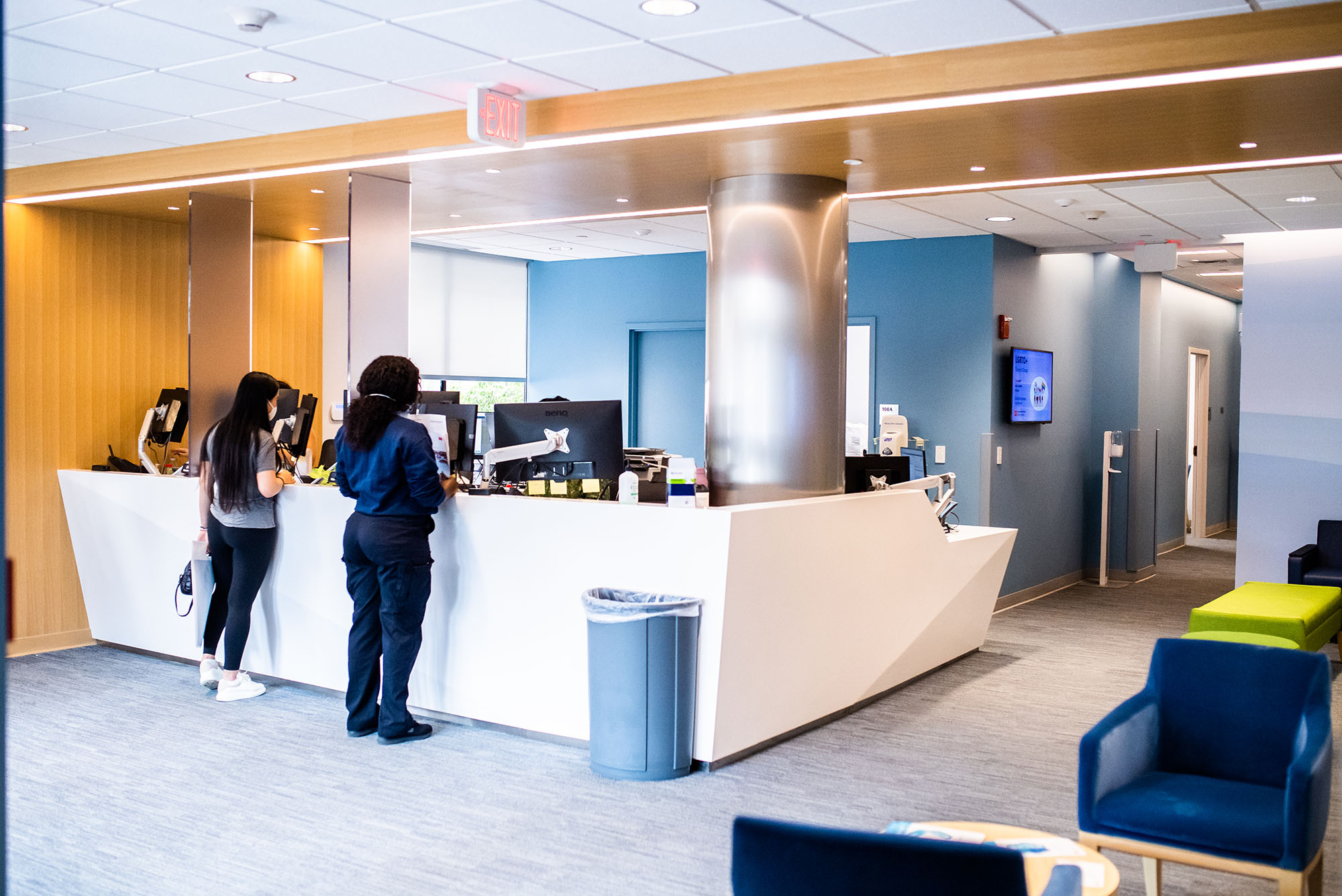 Photo: A stock photo of the updated Student Health Services. Two people stand at a front desk in spacious, clean white and blue waiting area.