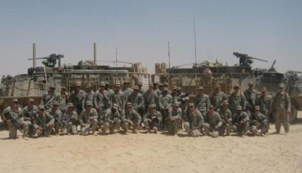 Photo: A group of US army people stand and pose for a large group photo in front of various army tanks and equipment.