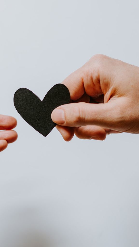 Photo: A small child's hand is shown giving a small, black paper heart to an elderly person's hand.