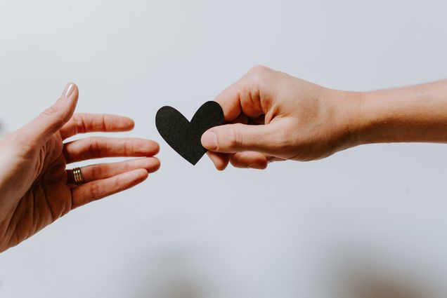 Photo: A small child's hand is shown giving a small, black paper heart to an elderly person's hand.