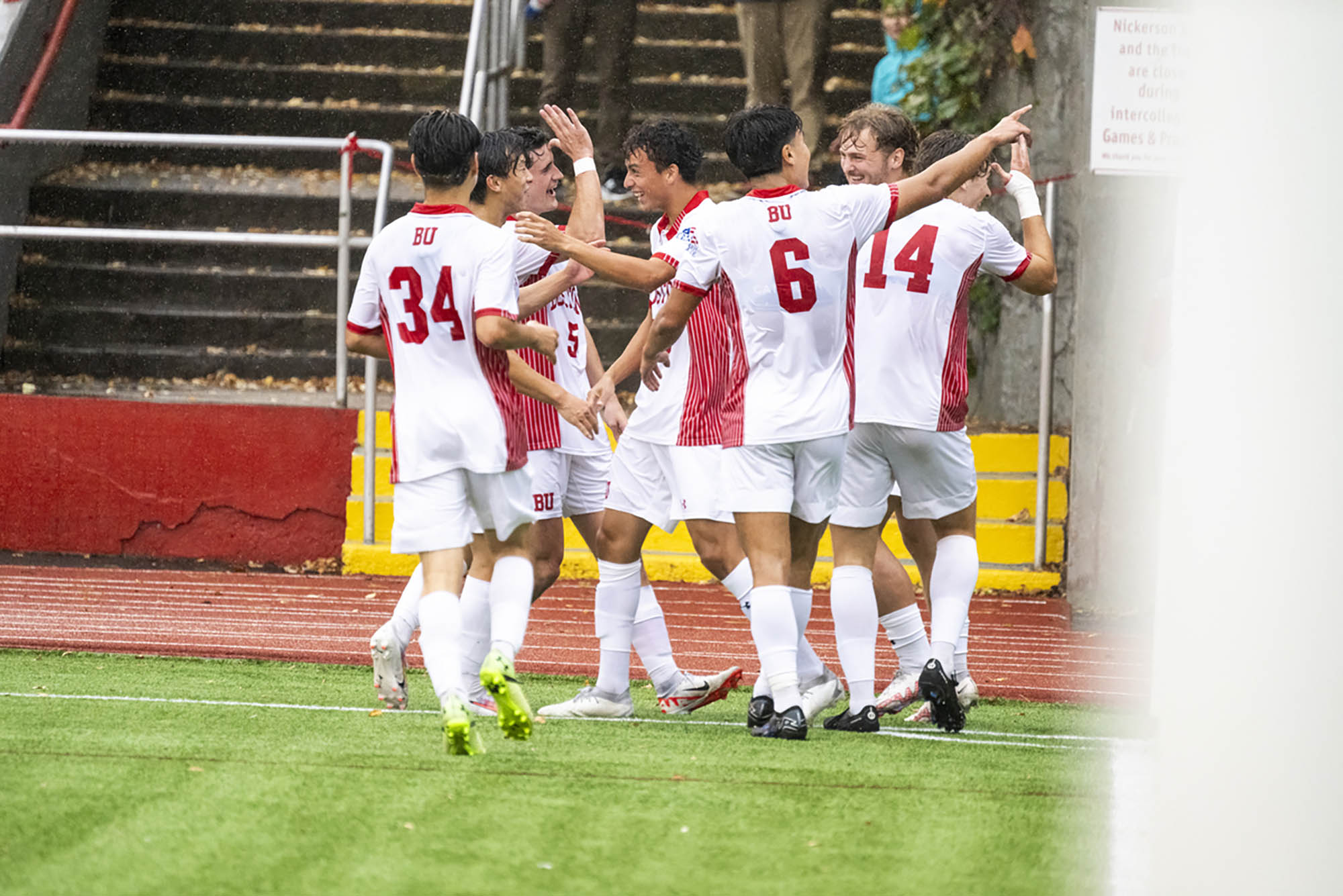 Photo: Five BU soccer players celebrate on the field as it rains. They are excited and embracing one another.