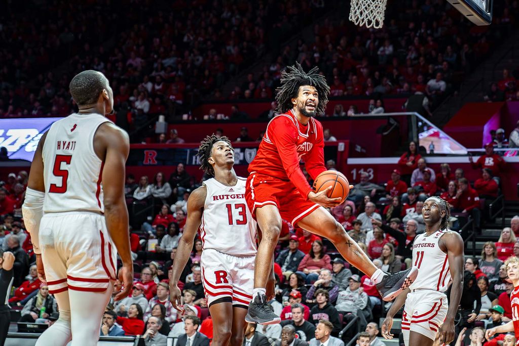 Photo: Player Miles Brewster (CAS’24), dressed in his red uniform, goes to windmill dunk the ball. The players from Rutgers, the other team, look on as he soars.