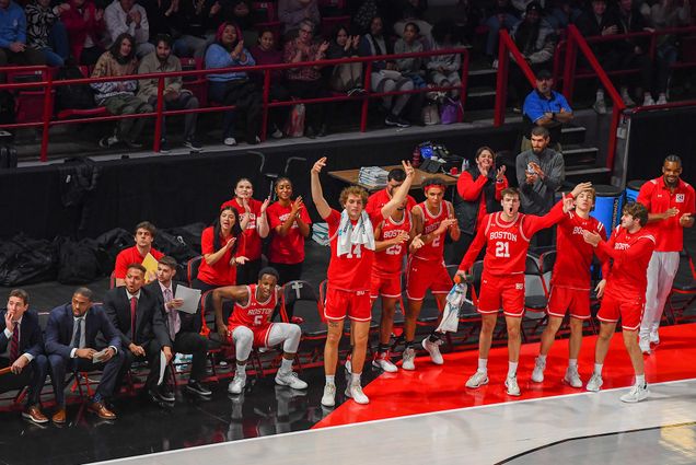 Photo: A photo of the men's basketball team on the sidelines cheering after a team member made a bucket. They wear their red uniforms.