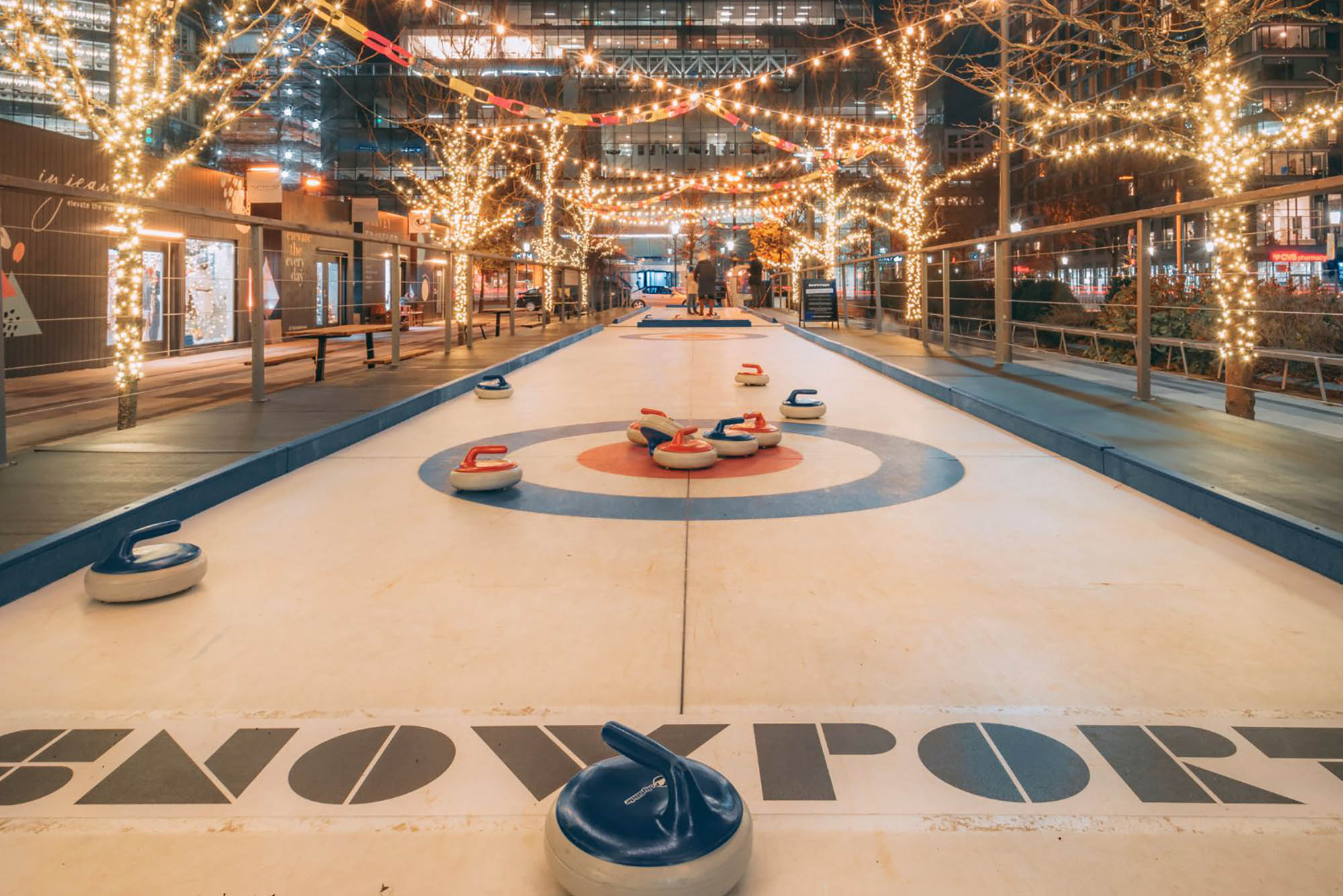 Photo: Fairy lights scatter across the trees lining the SnowPort curling lanes. The lanes are marked with the proper circles for the game with the SNOWPORT logo at the bottom center.