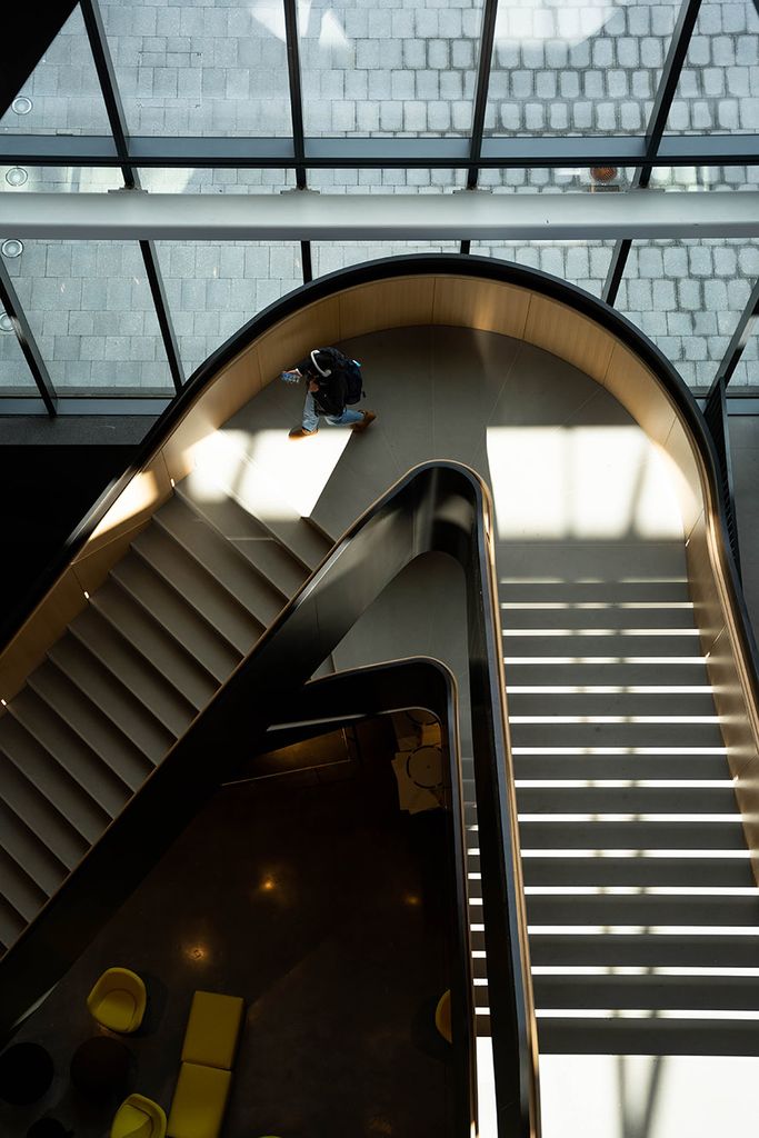 Photo: Overhead shot of students walking and gathering in and around a large set of black and wood butterfly stairs.