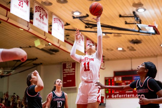 Photo: Caitlin Weimar goes to make a basket. She wears her white uniform and is playing in one of BU's gyms.