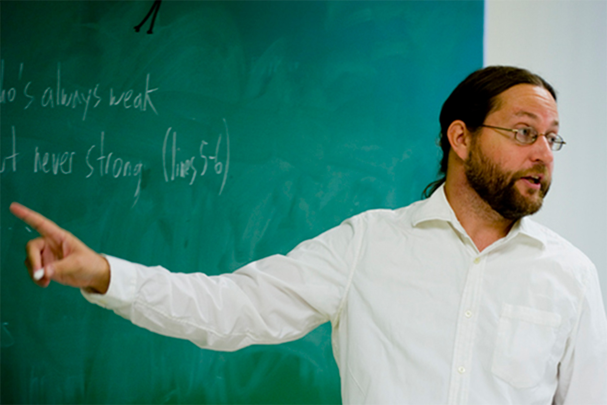 Photo: A professor in a white collared shirt teaching a class in front of a chalkboard