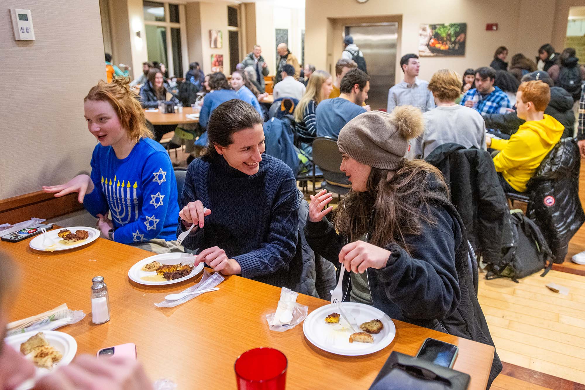 Photo: Three individuals giggle and smile over their plates of Latkes at BU's Latkepalooza.