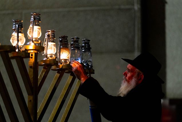 Photo: Rabbi Shnuel Posner lights the Menorah in front of the George Sherman Union. The menorah is taller than him, wooden, with lanterns as the lights.