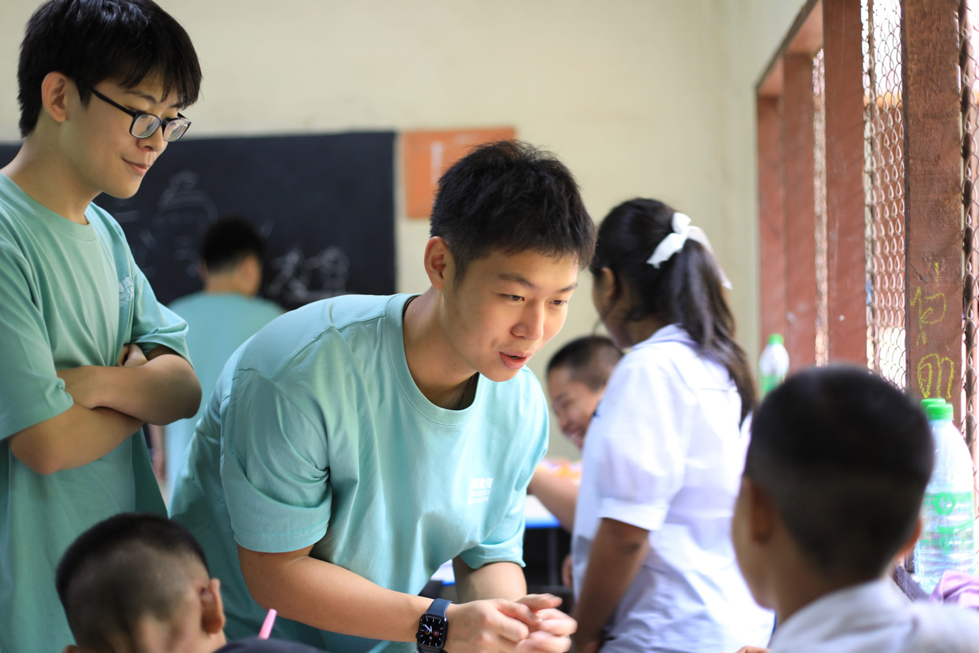 Photo: John, an Asian man, wears a light blue shirt and talks to kids as they look at him to ask questions.