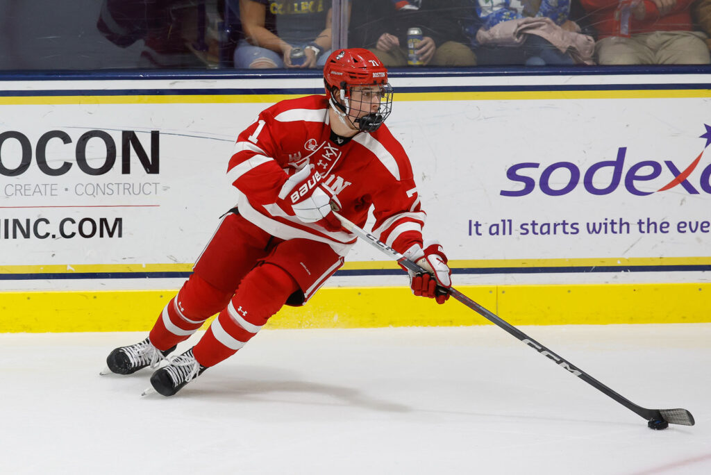 Photo: Macklin, a white man, skates on the ice in BU's red uniform for the hockey team.