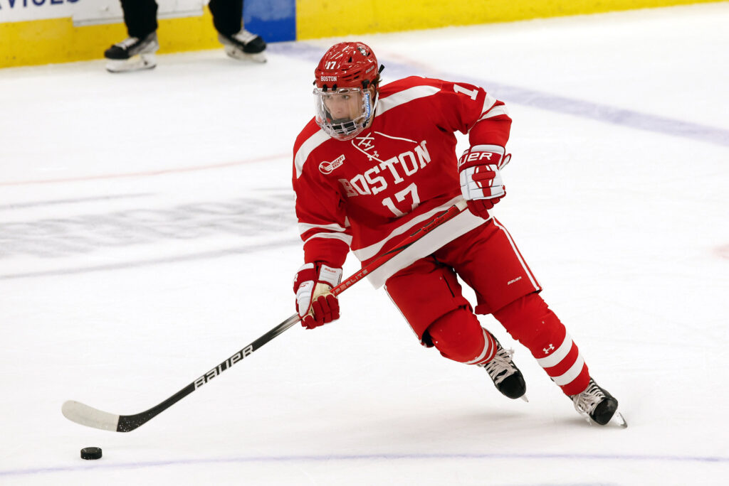 Photo: Quinn, a white man, skates on the ice in BU's red uniform for the hockey team.