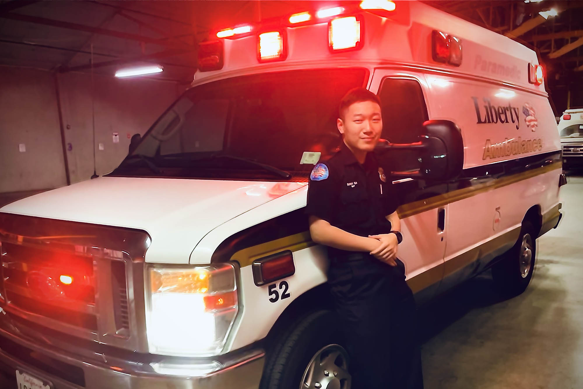 Photo: Sunny, a young Asian man, leans on an ambulance in his uniform for a photo.