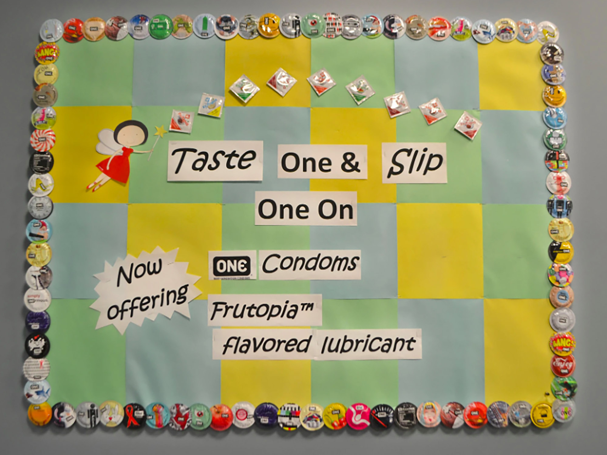 Photo: A bulletin board with checkered green, blue, and yellow backgorund. The text overtop reads "Taste One & Slip One On: Now offering ONE Condoms [and] Frutopia flavored lubricant".