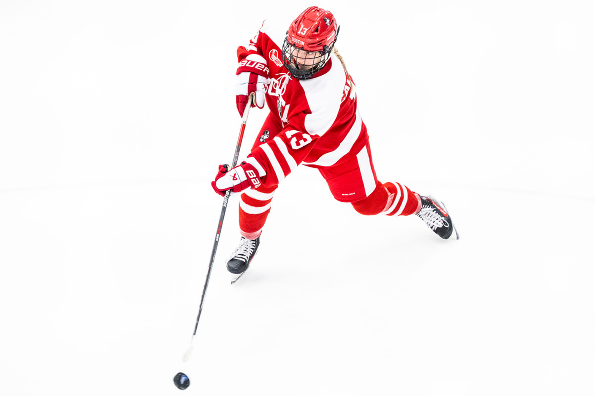 Photo: A BU women's hockey player in red and white uniform shoot the puck down the ice during a recent game