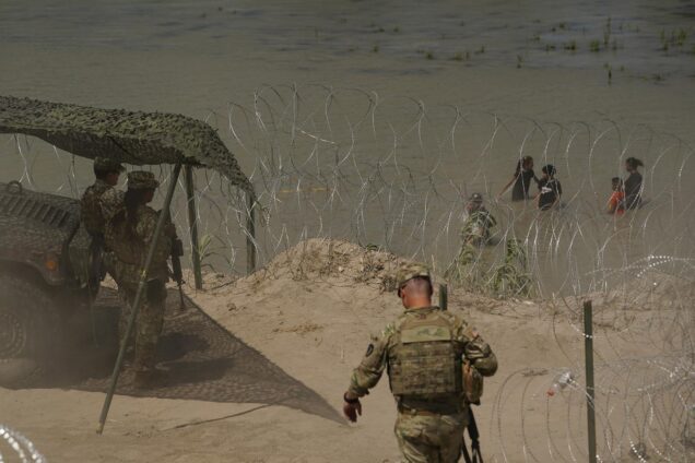Photo: Guardsmen watch as migrants try to cross the Rio Grande from Mexico into the U.S. They wear their military uniform.