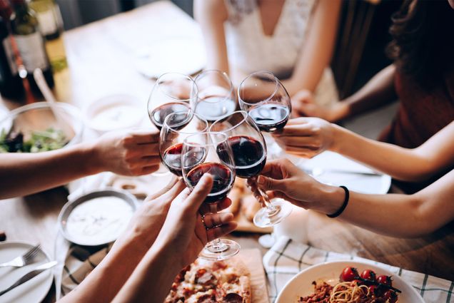 Photo: A group of people sitting at a table in a restaurant hold up their wine glasses for a toast.