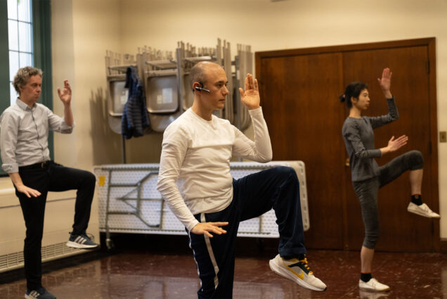 Photo: A man wearing headphones and casual workout attire guides a tai chi class with about 5-6 people following his movement