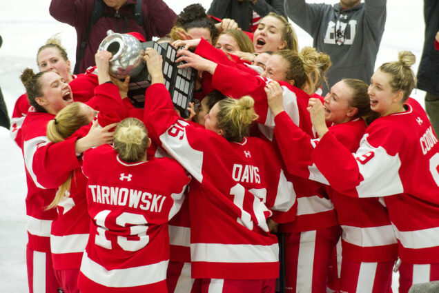 Photo: The BU Terriers celebrate with the Beanpot trophy after defeating Harvard in the Women's Beanpot Championship. The players are wearing red and white jerseys and hoisting a large spherical trophy