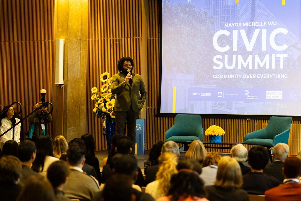 Photo: Nick Bates, a Black man, wears a suit and addresses the crowd at the Civic Center Summit.